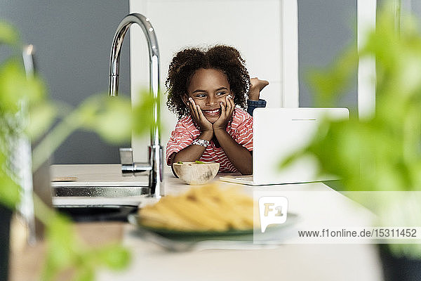 Happy girl with laptop in kitchen