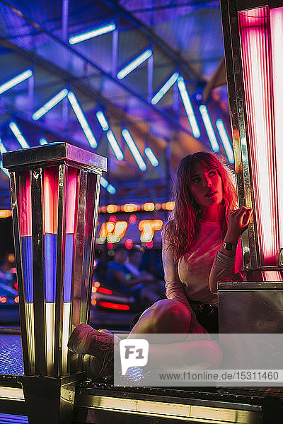Young woman sitting at the bumper car on a funfair at night