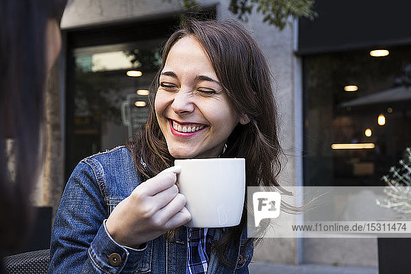 Happy young woman laughing with eyes closed and holding coffee cup in outside cafe in Madrid  Spain