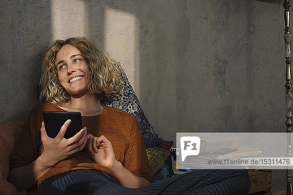 Portrait of happy young woman lying on bed using E-book reader