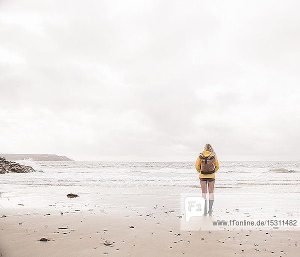 Rückansicht einer am Strand stehenden Frau in gelber Regenjacke