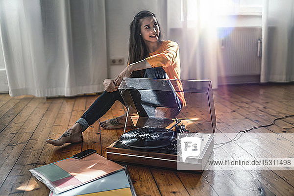 Junge Frau sitzt zu Hause auf dem Boden mit einem Plattenspieler