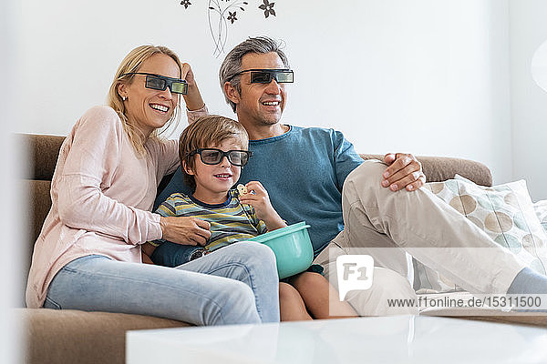 Father  mother and son wearing 3d glasses on couch at home watching Tv