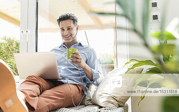 Mature man sitting on couch using laptop drinking coffee