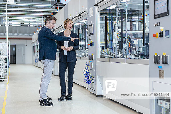 Geschäftsmann und Geschäftsfrau betrachten eine Maschine in einer modernen Fabrikhalle
