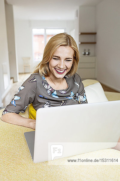 Laughing young woman using laptop on couch at home