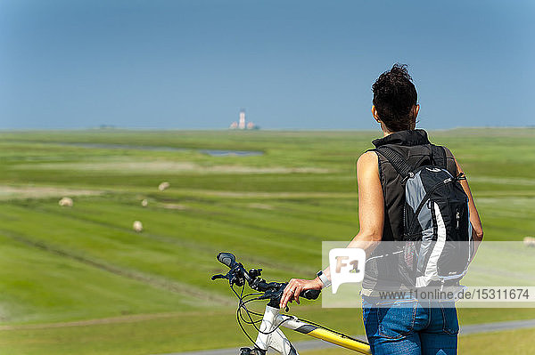 Deutschland Schleswig-Holstein Sankt Peter-Ording Frau mit Fahrrad die in die Ferne schaut