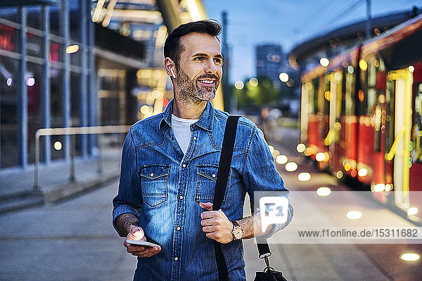 Mann hört Musik  während er während des abendlichen Pendelns nach der Arbeit auf die Straßenbahn wartet
