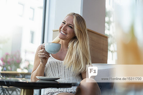 Porträt einer glücklichen blonden Frau  die in einem Café Kaffee trinkt