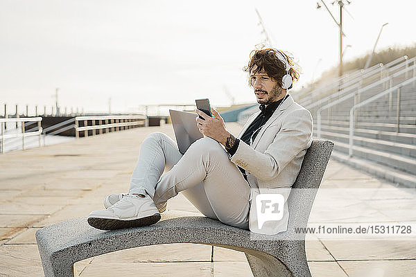 Portrait of shocked businessman with headphones and laptop looking at his mobile phone