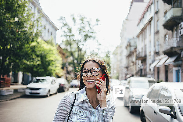 Glückliche junge Geschäftsfrau  die auf der Straße mit dem Handy telefoniert