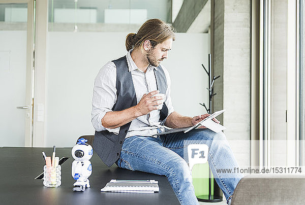 Junger Geschäftsmann sitzt im Büro mit Tablette und Tasse Kaffee auf dem Tisch