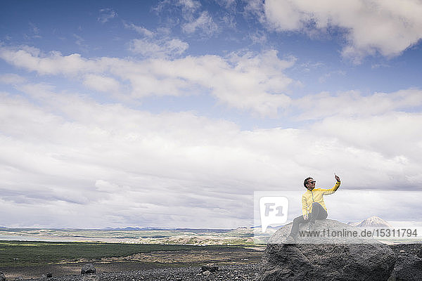 Junge Frau sitzt auf einem Felsen in Myvatn  Island  und nimmt sich