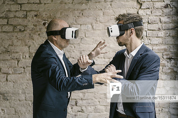 Senior and mid-adult businessman wearing VR glasses fighting