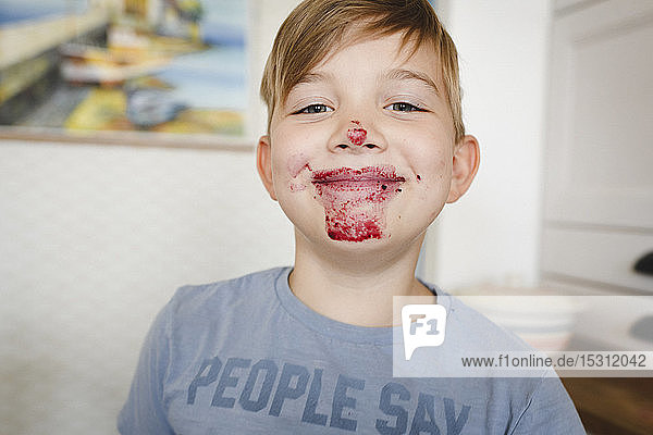 Porträt eines grinsenden Jungen mit Heidelbeermarmelade im Gesicht