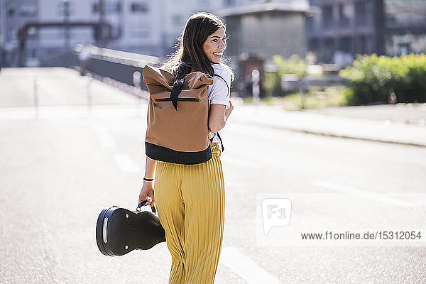 Glückliche junge Frau mit Geigenkoffer auf der Strasse