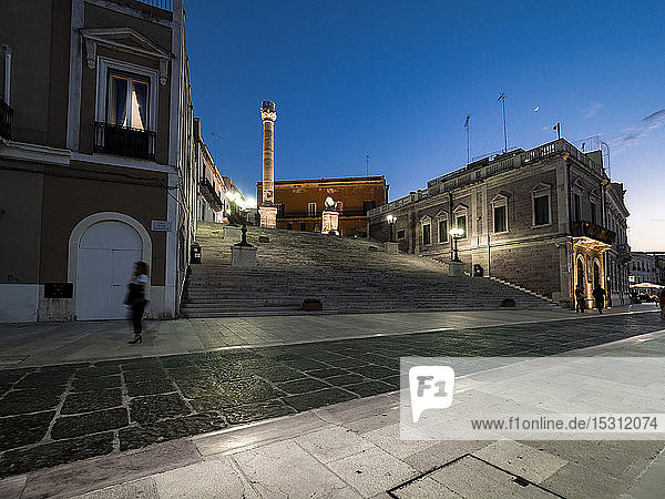Beleuchtete römische Säule auf Stufen inmitten von Gebäuden in Brindisi gegen den nächtlichen Himmel