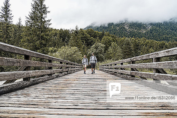 Young couple on a hiking trip walking on wooden bridge Vorderriss Bavaria Germany