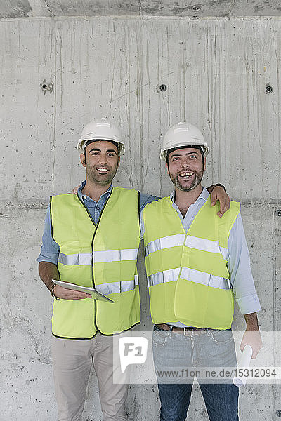 Porträt von zwei männlichen Arbeitern mit einer Tafel auf einer Baustelle