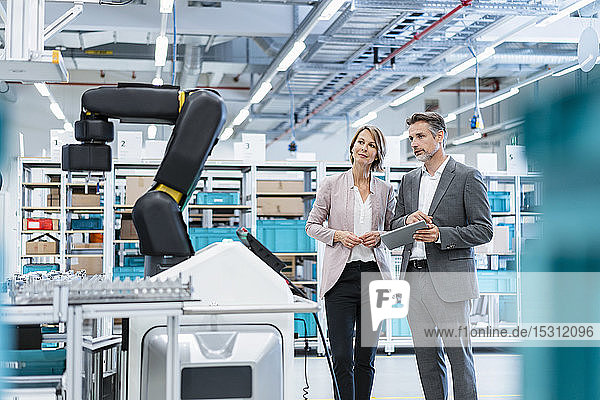 Geschäftsmann und Geschäftsfrau in einer modernen Fabrikhalle mit Blick auf Roboter