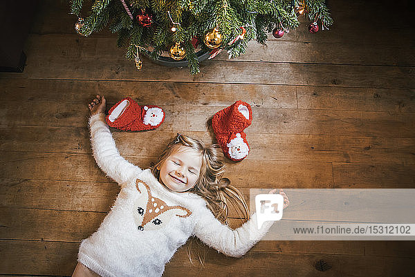 Smiling girl with closed eyes lying under the Christmas tree