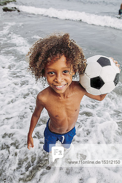 Porträt eines lächelnden Jungen  der am Strand einen Fussball hält