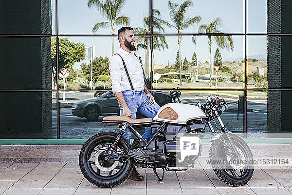 Mann mit Motorrad vor Glasfassade stehend