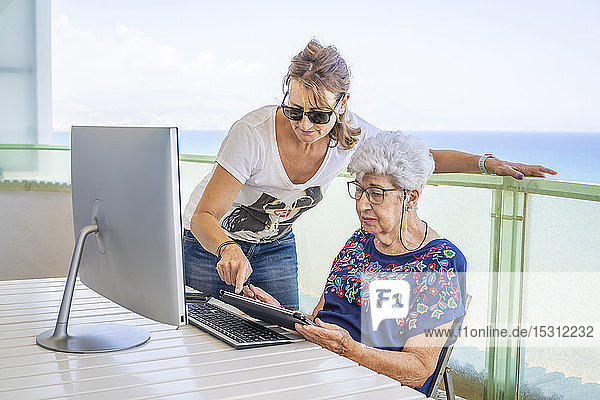 Ältere Frau mit Tablette auf der Terrasse  unterstützt von ihrer Tochter