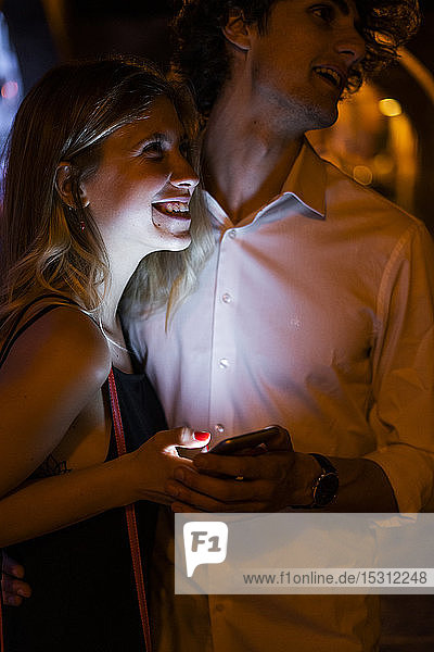 Glückliches junges Paar mit leuchtendem Handy in der Nacht