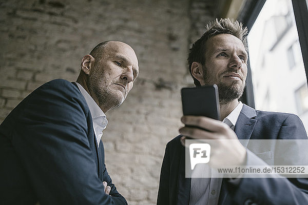 Mid-adult businessman holding cell phone with senior businessman behind him