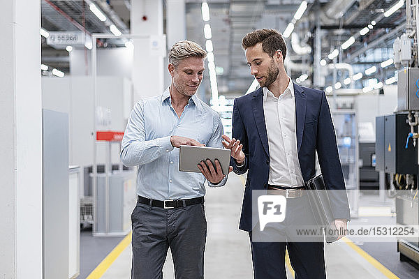 Two businessmen with tablet talking in a modern factory