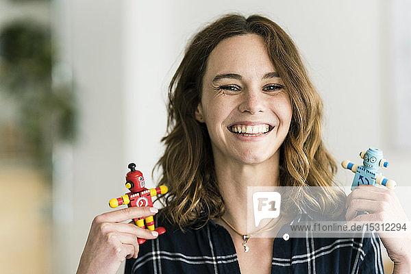 Lachende Frau hält männliche und weibliche Spielzeugroboter