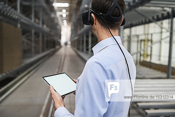 Businessman with tablet wearing VR glasses in factory