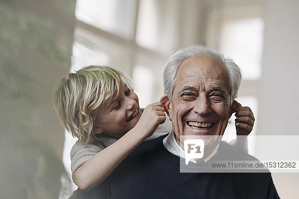 Happy grandson pulling grandfather's ears at home