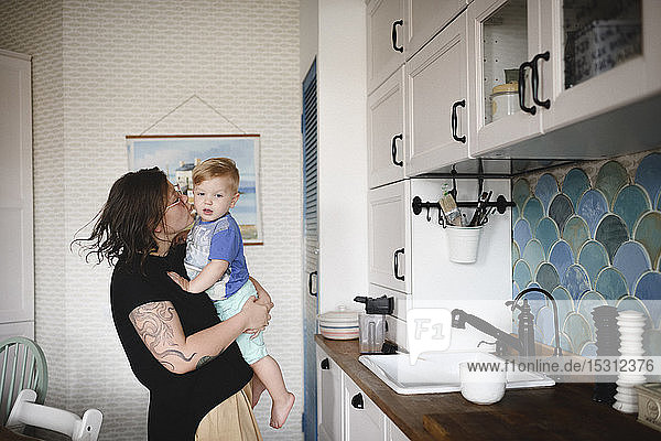 Mutter trägt ihren kleinen süßen Sohn in der Küche