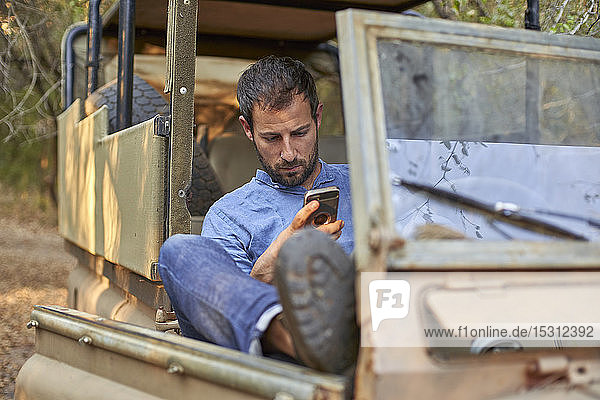Man sitting in by off-road car  using smartphone