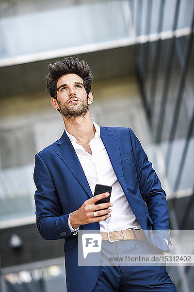Geschäftsmann mit Mobiltelefon vor einem Bürogebäude