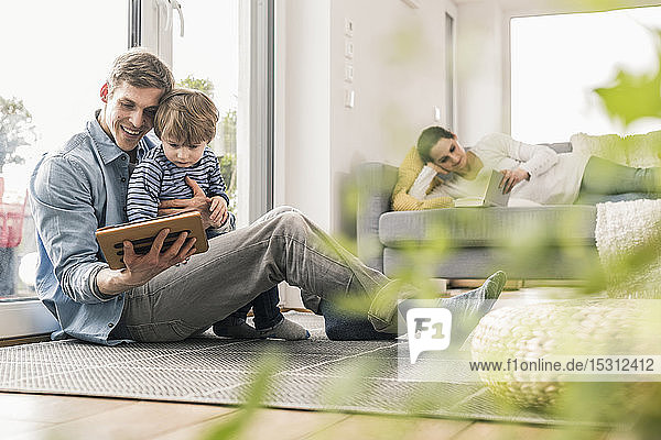 Vater und Sohn liegen auf dem Boden und benutzen ein digitales Tablett