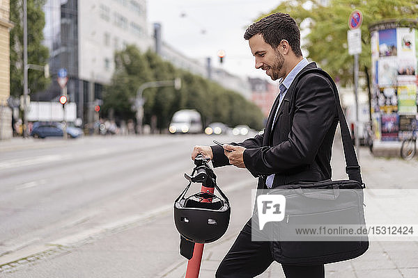 Geschäftsmann mit E-Scooter mit Mobiltelefon in der Stadt