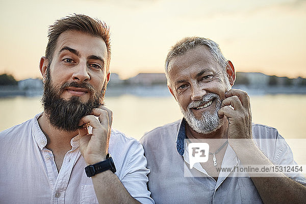 Porträt eines lächelnden Vaters und eines erwachsenen Sohnes  die sich am Bart kratzen
