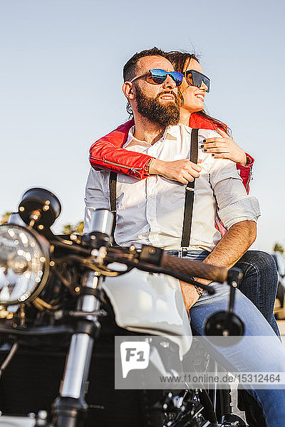 Porträt eines Paares  das in der Abenddämmerung auf einem Motorrad sitzt und in die Ferne schaut