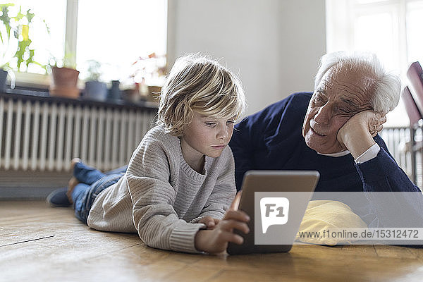 Grandfather and grandson lying on the floor at home using a tablet