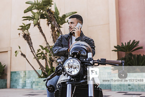 Porträt eines jungen Mannes am Telefon  der auf seinem Motorrad sitzt