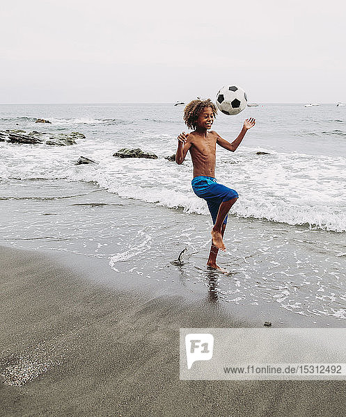 Junge spielt mit einem Fussball am Strand