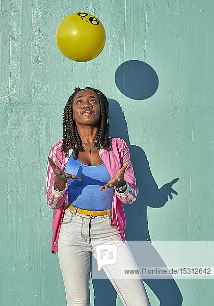 Young black woman playing with a color ball in front of a blue wall