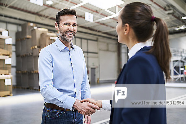 Businessman and businesswoman shaking hands in a factory