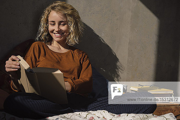 Portrait od smiling young woman sitting on bed reading a book