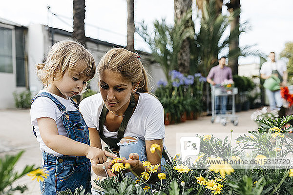 Mitarbeiterin eines Gartencenters zeigt einem kleinen Mädchen Blumen