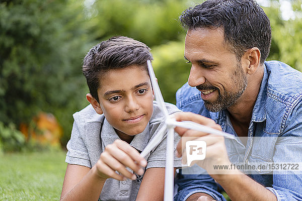Smiling father and son lying in garden with a wind turbine model