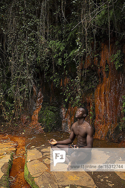 Junger Mann meditiert an einem Wasserfall